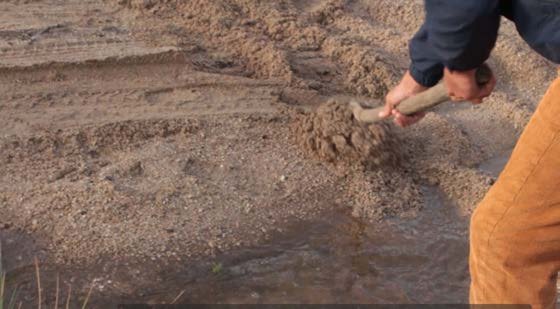 Hands moving earth with a rake beside the water.
